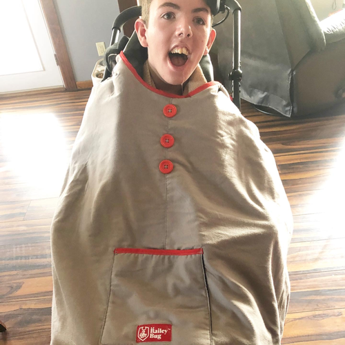 Bailey smiling in a wheelchair while wearing a tan Bailey Bug coat