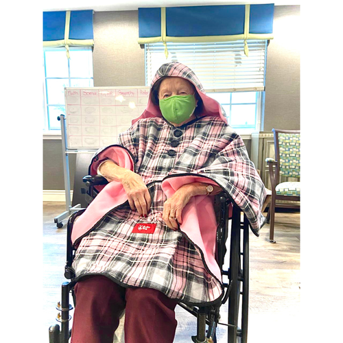 A resident smiling in a wheelchair while wearing a pink plaid Bailey Bug coat